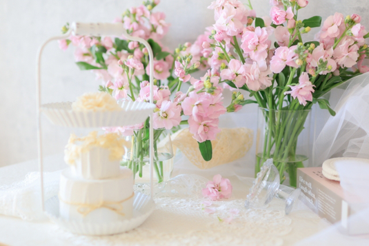 オレンジのガーベラや小手毬の花が活けられた休日のテーブル。紅茶の入ったカップ&ソーサ。ケーキの載った皿。