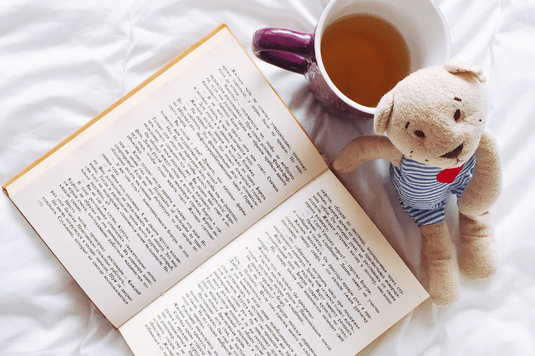ページが開かれた洋書。紅茶のはいったマグカップにもたれかかるように置かれたクマのぬいぐるみ。