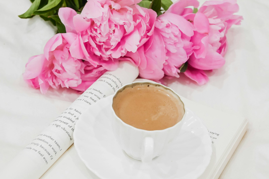 ピンクの大輪のシャクヤクの花。ページが広げられた洋書のうえに置かれたコーヒーのカップ＆ソーサ。