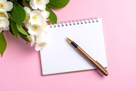 リングメモとボールペン。白色の花とグリーンの小枝。
