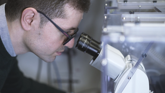Chercheur observant au microscope lors du tournage d’un film institutionnel scientifique