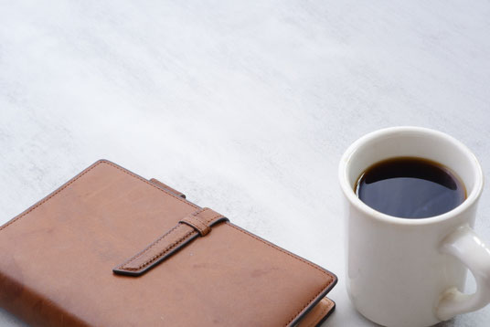 茶革のシステム手帳とコーヒーの入ったマグカップ。