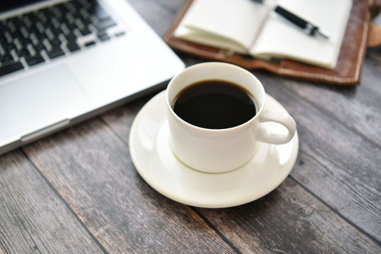 木目のデスクにノートパソコンとコーヒーの入ったカップ＆ソーサ。傍らに革張りの手帳が広げられている。