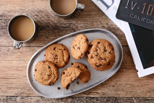 積まれた雑誌。コーヒーのマグカップ。チョコチップクッキーが盛り付けられたお皿。