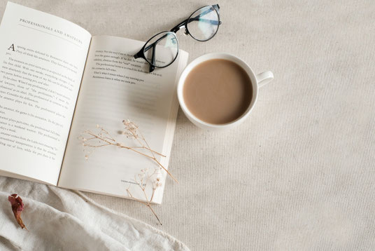 ページがめくられた洋書。黒ぶち眼鏡。カフェオレのマグカップ。ドライフラワー。