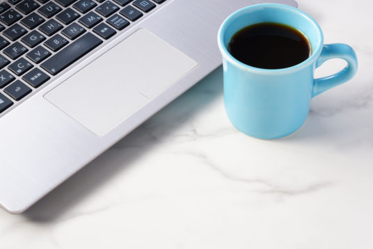 ノートパソコンの前にコーヒーの入った水色のマグカップが置かれている。