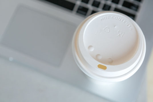 ノートパソコンのキーボードの上に置かれたテイクアウトコーヒー。