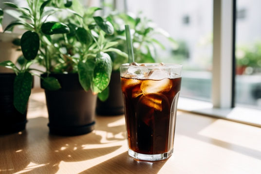 オフィスの窓辺に飾られたグリーンの鉢植たち。隣に置かれたアイスコーヒーのグラス。
