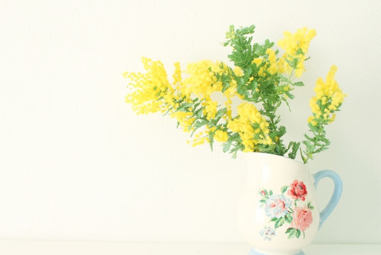 バラの花が描かれた花瓶に生けられたミモザの花。