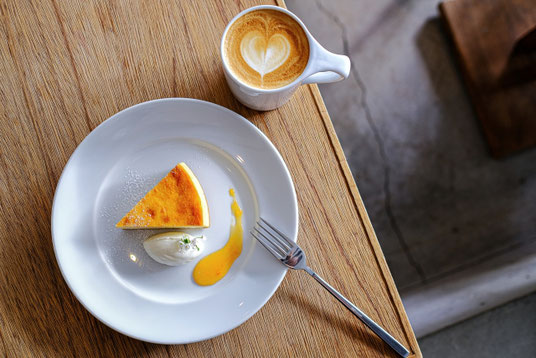 カフェのテーブル。チーズケーキのお皿とフォーク。ラテアートが描かれたコーヒーのマグカップ。