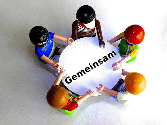 Fünf Lego-Figuren sitzen gemeinsam an einem runden Tisch, um zusammen zu arbeiten