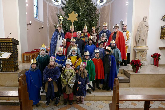 Wir seehen die Sternsingergruppe nach der Aussendungsfeier am 3. Januar 2026 auf den Stufen vor dem Altar in der Kirche St. Josef zusammen mit Pfr. Holger Schmitz