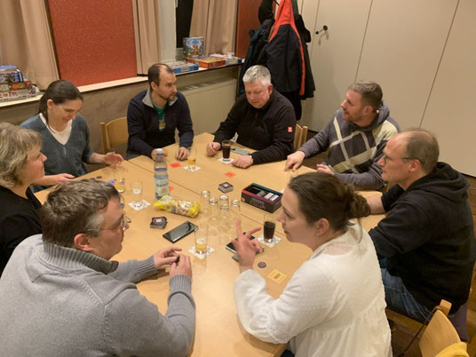 Das Foto zeigt acht Personen an einem Tisch während des Spieleabends bei Spiel und Gesprächen
