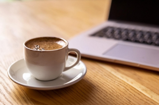 ノートパソコンの前に置かれたコーヒーの入ったカップ＆ソーサ。