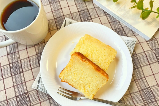 格子柄のクロスが敷かれたテーブル。パウンドケーキのお皿とフォーク。傍らに本。コーヒーの入ったマグカップ。