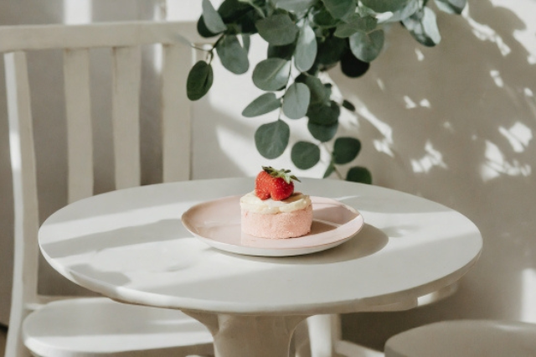 白の丸テーブルに置かれたいちごケーキのお皿。ユーカリの小枝。お休みの日。