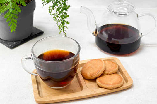 トレイにのったクッキーと紅茶のカップ。ティーポットとグリーンの鉢植。