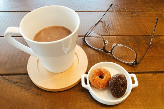 飲みかけのコーヒーカップとドーナツのお皿。傍らに黒ぶち眼鏡が置かれている。