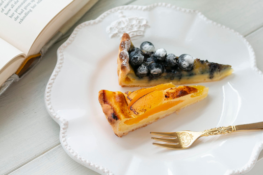 カフェテーブルに広げられた本。タルトケーキがのったお皿と金色のフォーク。サービス業。