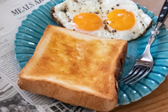 英字新聞の上に置かれた朝食プレート。トーストパンと目玉焼き。