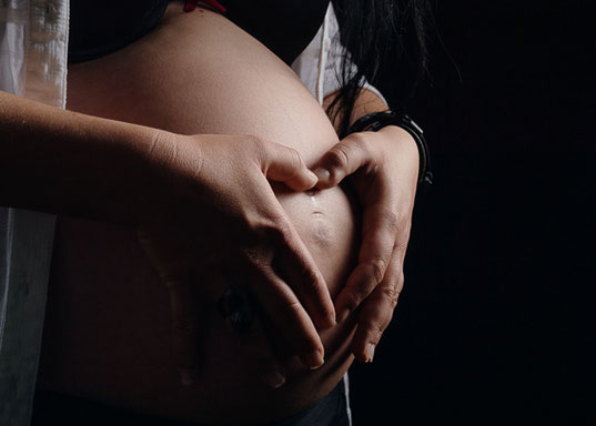 Nahaufnahme von Händen, die den Babybauch sanft halten, stimmungsvolles Studiolicht