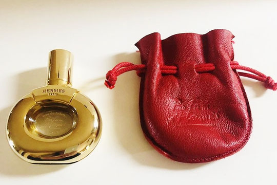HERMES - PARFUM D'HERMES EAU DE TOILETTE : FLACON METAL DORE DANS POCHON CUIR ROUGE