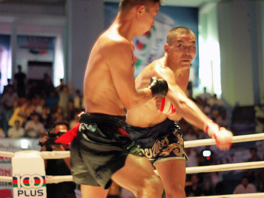 Im Boxring sind zwei asiatische Boxer, die Lethwei kämpfen. Sie haben nur Thaiboxhosen an und bandagierte Fäuste.