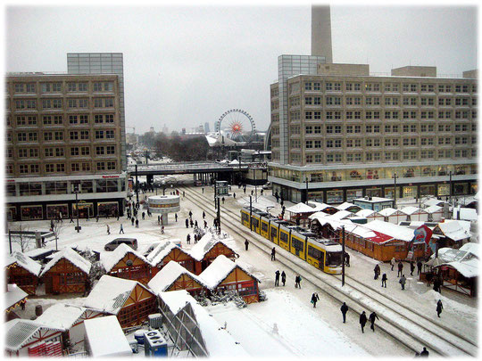 Bilder vom Alexanderplatz in Berlin mit der neuen gelben Tram und einem Weihnachtsmarkt. Im Hintergrund sieht man ein Riesenrad des Weihnachts-Rummels.