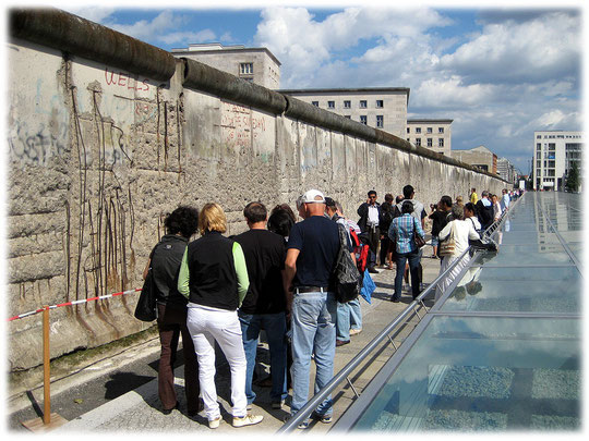 Das Bild zeigt Touristen aus aller Welt, die Fotos und Bilder von den Resten der Berliner Mauer aufnehmen. Rechts sind die Folterkeller der Nazis sichtbar.