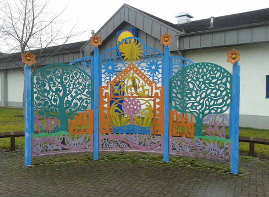 Multicoloured metal sculpture by Lidl. Their store developments are often accompanied by public art. This was damaged by a vehicle c. 2023, was stored for a while and now appears to have been permanently removed. One post still stands forlornly.