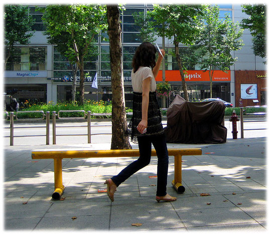 Pictures of a young Korean woman hiding her face behind some paper to avoid getting tanned. Bilder von jungen Frauen die nicht ihr Gesicht in die Sonne stecken möchten