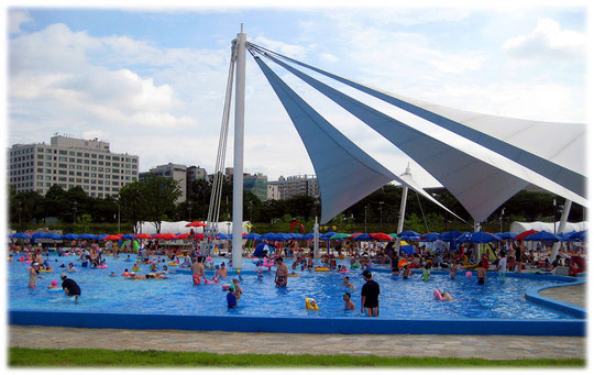 On this photo you see an open air public swimming pool full of city life. Foto von einem öffentlichen Schwimmbad und Freibad. Die koreanischen Kinder spielen und schwimmen wild umher.