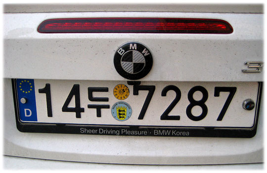 This photo shows a Korean car sign with German blue national sign at the side. Bild von einem deutschen BMW Auto PKW in den Straßen von Seoul in Südkorea.