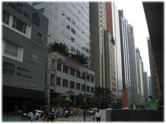 This image is about a narrow street in Seoul, on the left and on the right are really high buildings which cause shadow for the street. Bilder von Hochhäusern die eine Straße mit Schatten bewerfen