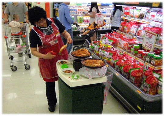 A Korean woman prepares fresh free trials of Korean food dishes inside the shop. The customers can try all meals. Koreanisches asiatisches Essen in einem asiatischen Markt in Südkorea. American food.