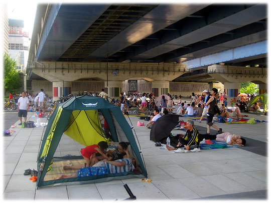 This image shows many people of Seoul sitting beneath a bridge at Han river park. They try to avoid the sun! Foto von Koreanern die unter einer Brücke im Schatten sitzen.