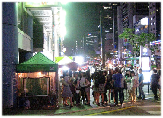Pictures of a long row of young women standing at a street fortune tellers tent and waiting to find answers about their future. Bilder von jungen Koreanerinnen die beim Wahrsager warten