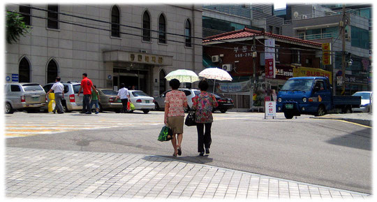 Pictures of two Korean women walking in the sunshine. But they protect their white skin with lovely sunshades in South Korea. Ein Foto von Frauen die in Südkorea Sonnenschirme tragen.