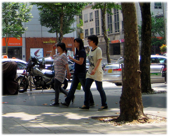 This photo shows city people walking in the shadow and hiding their face from the sun. Bild von jungen Koreanerinnen die sich vor der Sonne schützen
