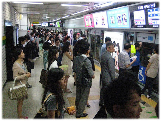 Picture with Koreans waiting at subway train sliding glass doors for the train to come. Bild mit Koreanern in U-Bahn-Station.