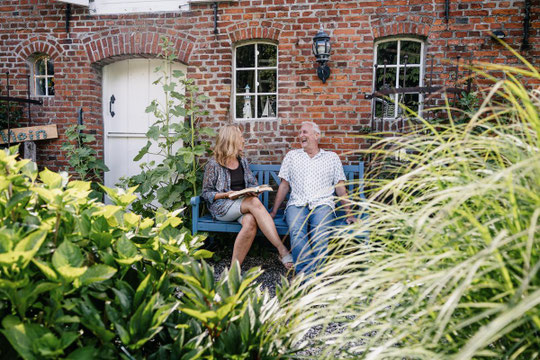 Lachendes Paar im Urlaub vor typischem Reetdachhaus in Nordfriesland.