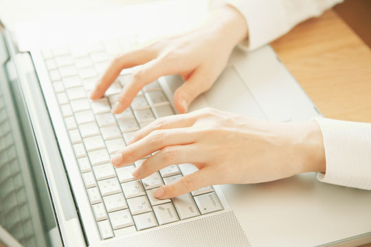 ノートパソコンのキーボードを叩く女性の指先。