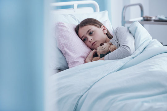 Mädchen im Krankenhausbett mit Trösterbär im Arm