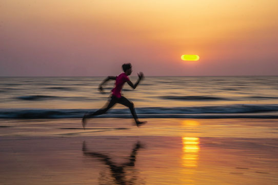 Ein Mann in Sportkleidung rennt am Strand bei Sonnenuntergang im Hintergrund.