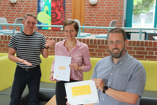 Bild: Dr. Jerome Biehle (Schulleiter), Mette Woidke (Schülersprecherin), Claas Niehues (MINT-Koordinator) mit Urkunde und Schild zur Auszeichung als Digitale Schule.
