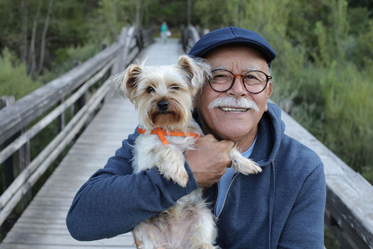 Älterer Herr hält beim Spaziergang in der Natur gut gelaunt seinen kleinen Hund auf dem Arm