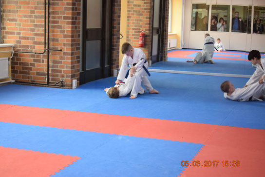 Selbstverteigungsübungen in der Taekwondo-Kindergruppe. Zwei Jungs trainieren die Selbstverteidigung. Ein Junge liegt am Boden und der zweit Junge hält ihn fest.