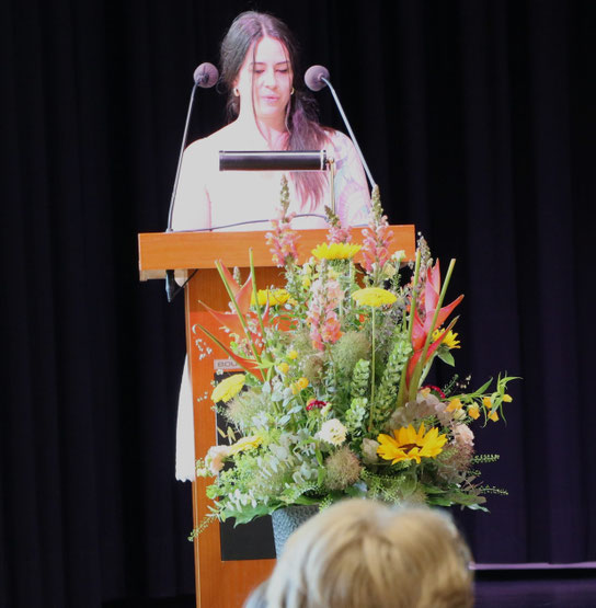 Jennifer_de_Biasio_am_Rednerpult_mit_vielen_Blumen