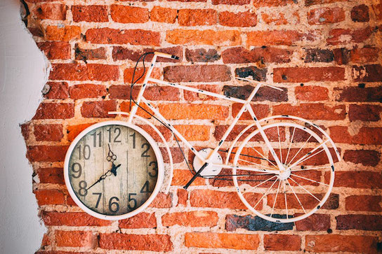 レンガ調の壁紙に自転車の絵が描かれている。車輪の部分に壁時計が掛けられている。