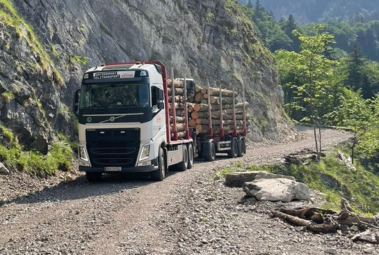 LKW beim Rundholztransport auf Schotterstraße am Berg